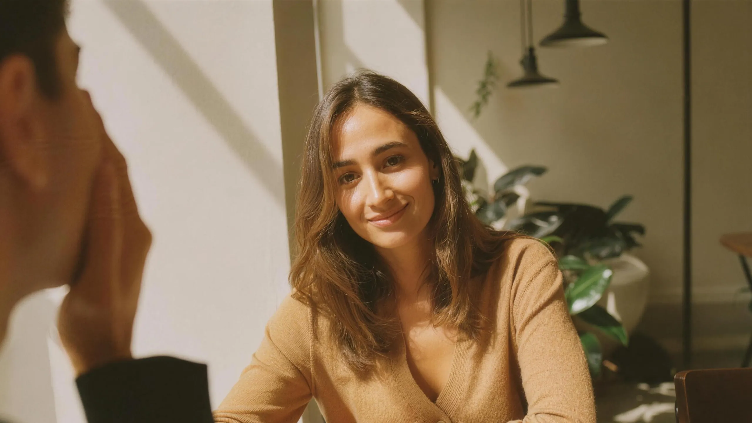 A client at a sunlit table with a coffee, smiling at the researcher across from her as they go through her quote.